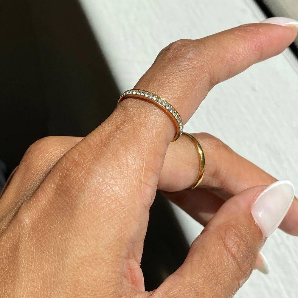 Close-up of a hand with two gold rings, one with small diamonds, in natural light