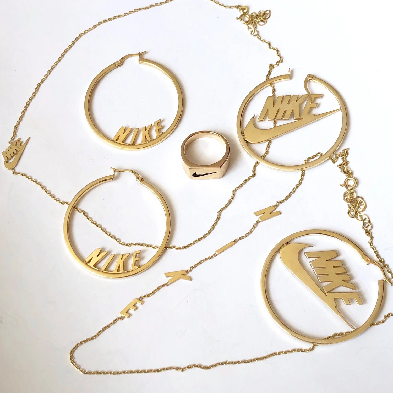 Gold Nike-themed jewelry set including hoop earrings, ring, and chain necklace on white background